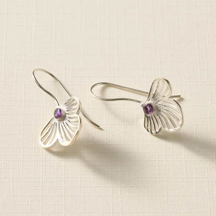 Silver earrings with purple gemstones on a beige textured background