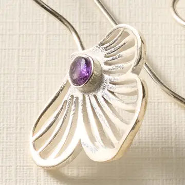 Silver earring with a purple gemstone on a textured beige background
