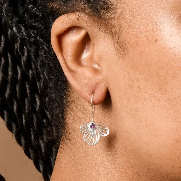 Close-up of an ear wearing a silver earring with a purple gemstone.