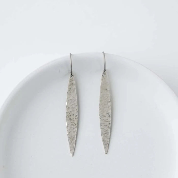 Pair of long, thin silver earrings on a white plate with a white background