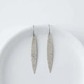 Pair of long, thin silver earrings on a white plate with a white background