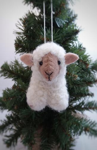 Handmade felt sheep ornament,  crafted from felted wool in beige and white colors, hanging in front of a green Christmas tree.