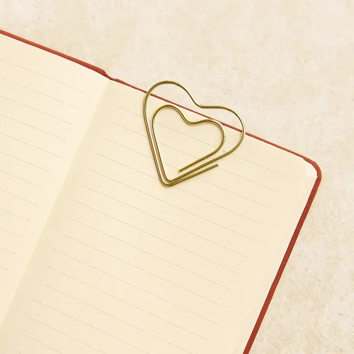 Heart-shaped gold paper clip on a lined notebook page with a beige background