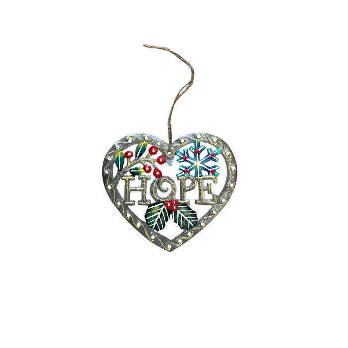 A heart-shaped metal Christmas ornament with the word 'HOPE' in the center, decorated with a snowflake, holly leaves, berries, and a hanging twine string, shown on a plain white background.
