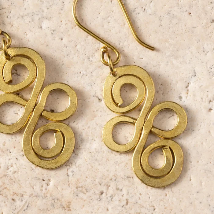 Gold spiral earrings on a beige stone surface
