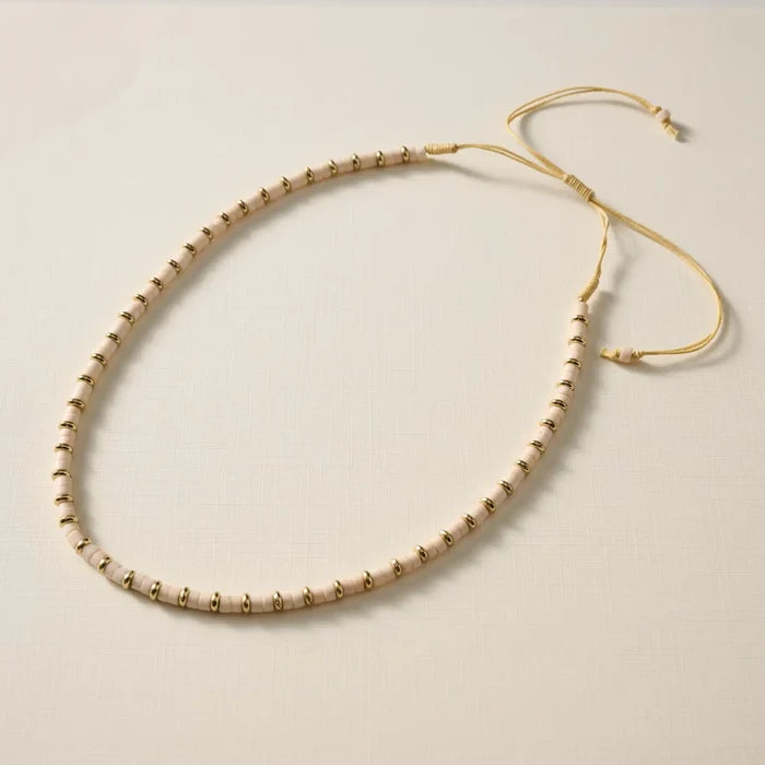 Beaded necklace with gold and beige beads on a light background