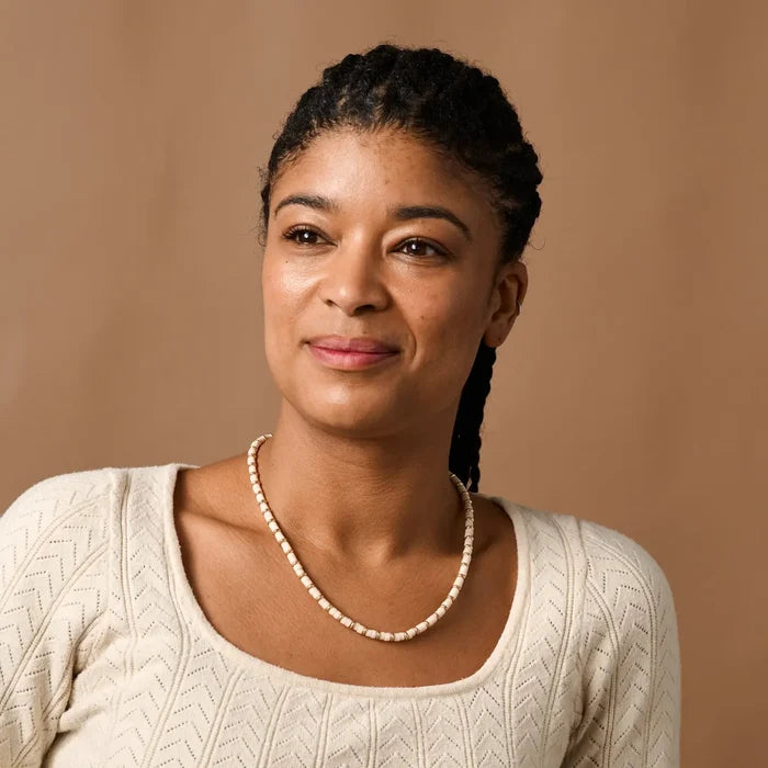 Woman wearing a beaded necklace against a brown background