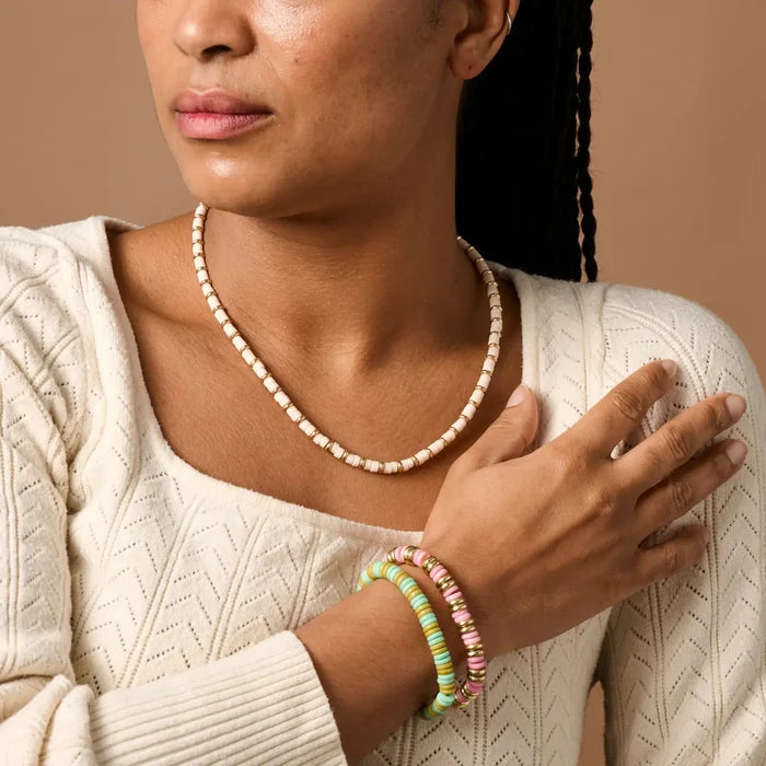 Woman wearing a beaded necklace and colorful bracelets on a beige background