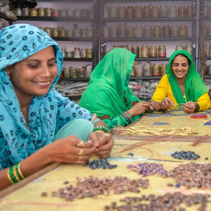 Three women in colorful headscarves working with beads in a workshop.