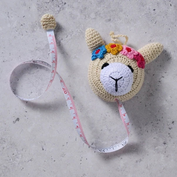 Crocheted llama measuring tape  on a concrete surface