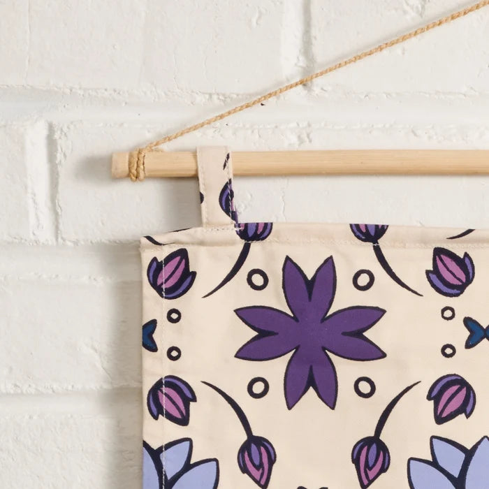 Floral patterned banner with purple flowers hanging on a white brick wall.