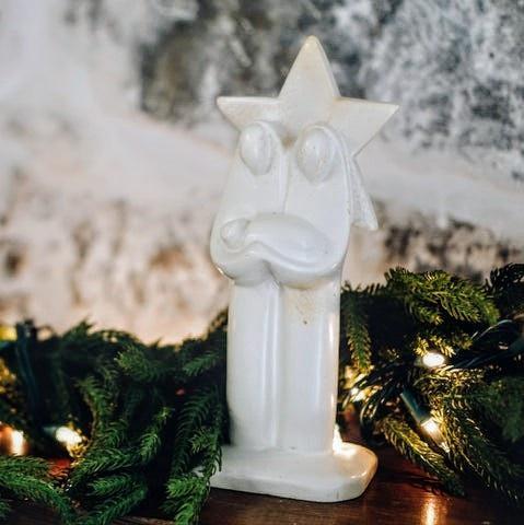 Hand carved white nativity scene with a star behind Mary and Joseph in front of a Christmas garland.