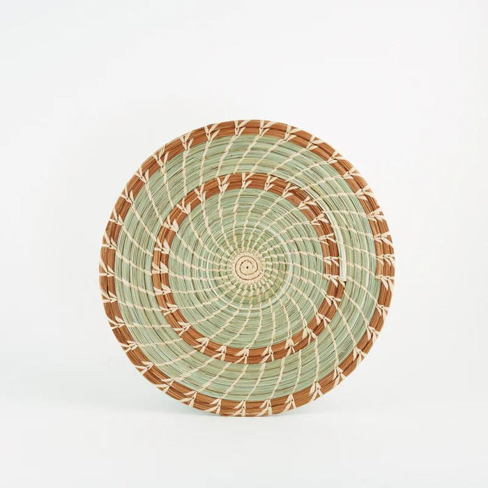 Handmade woven pine and grass trivet with brown and green spirals on a white background.