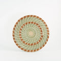 Handmade woven pine and grass trivet with brown and green spirals on a white background.