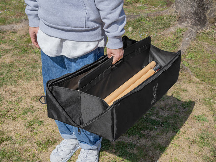 A person carrying an open black Pole Case by its reinforced inner handle, showcasing wooden poles stored in the internal compartments.