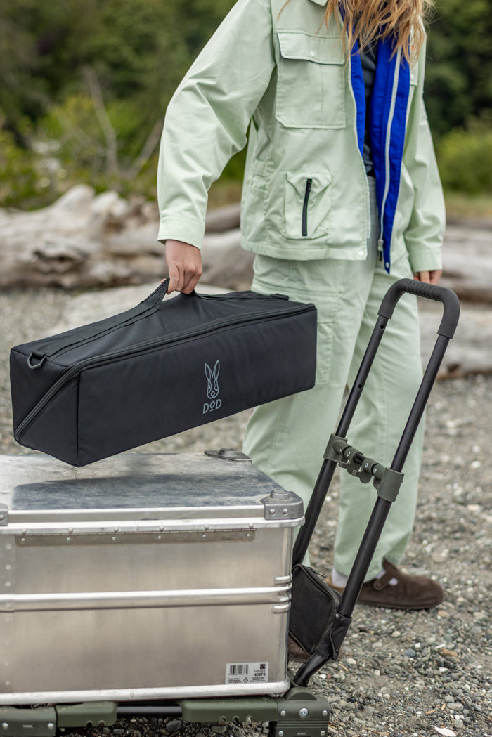 A person carrying the closed black Pole Case while standing next to a silver metal storage trunk in an outdoor setting.
