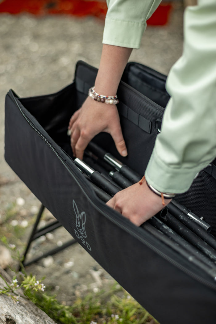 Close-up of a person's hands organizing black metal tent poles into the partitioned interior of the Pole Case.