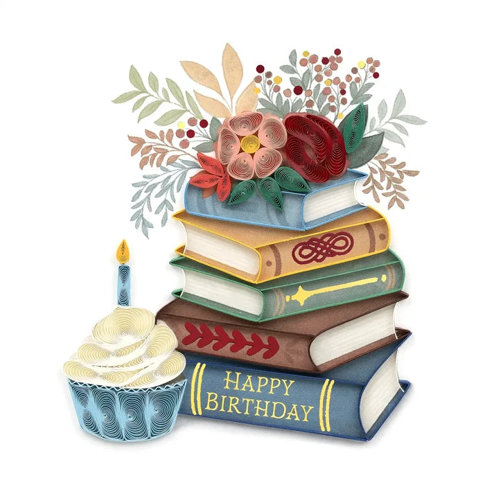 Stack of books with a 'Happy Birthday' message, cupcake, and floral arrangement on a white background