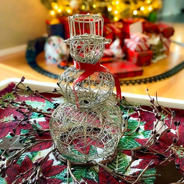 Decorative silver snowman on a Christmas-themed tablecloth with blurred festive background.