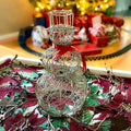 Decorative silver snowman on a Christmas-themed tablecloth with blurred festive background.