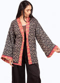 A woman modeling a black printed open-front jacket with red and gold patterned trim, paired with black pants, against a plain white background.