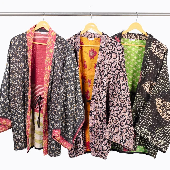 Three colorful patterned kimono-style jacket hanging on wooden hangers from a metal rail against a plain white background.