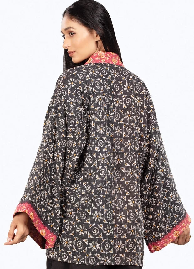 A woman shown from the back wearing a dark charcoal gray quilted jacket with a beige and gold floral block print and contrasting pink and gold patterned inner lining on the collar and cuffs.