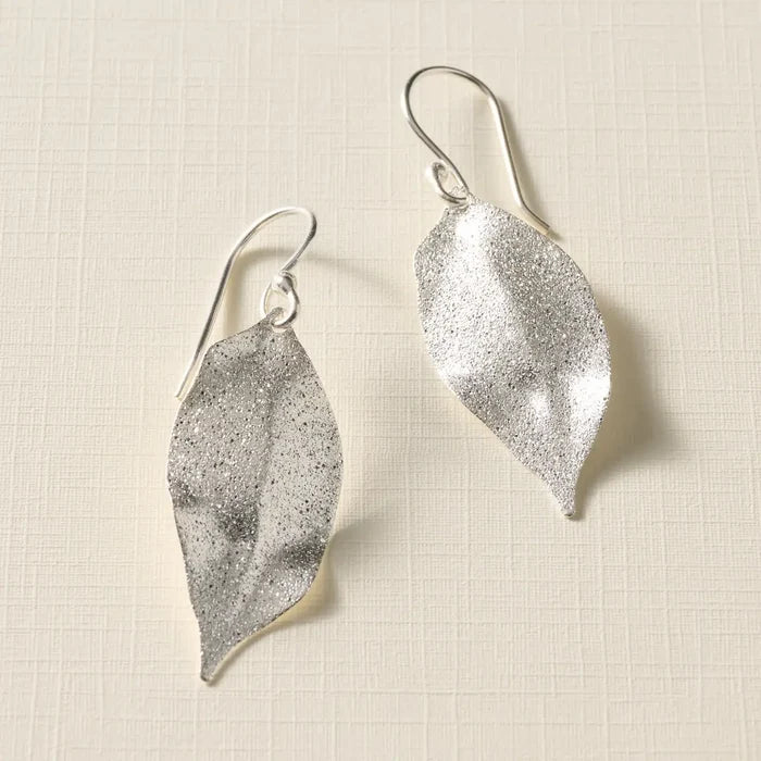 Silver leaf-shaped earrings on a textured beige background