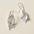 Silver leaf-shaped earrings on a textured beige background