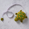 Crocheted turtle  measuring tape on a concrete surface