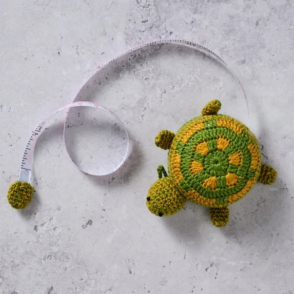 Crocheted turtle  measuring tape on a concrete surface