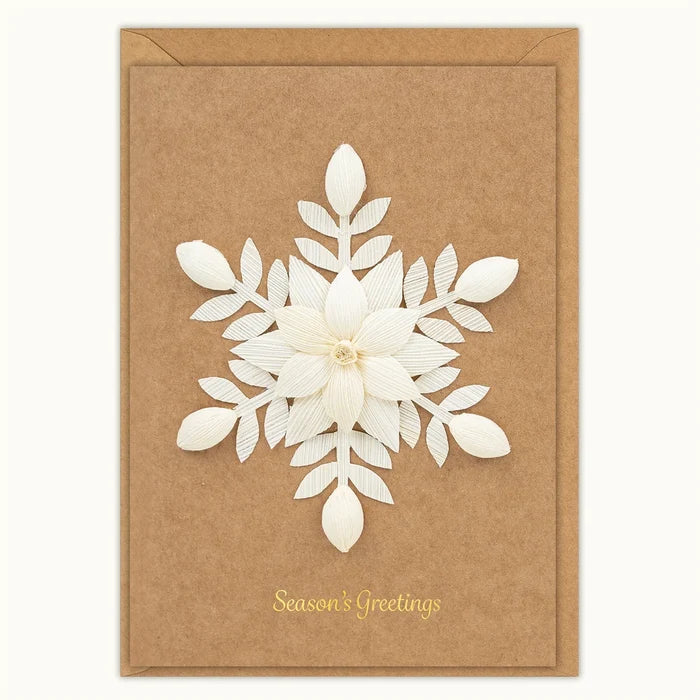 A rectangular kraft brown greeting card with a large white layered paper snowflake design in the center and gold 'Season's Greetings' text near the bottom, shown with a matching kraft envelope on a light neutral background.